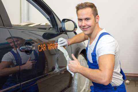 Car wrapping professional puts letters made of vinyl foil or film on vehicle door